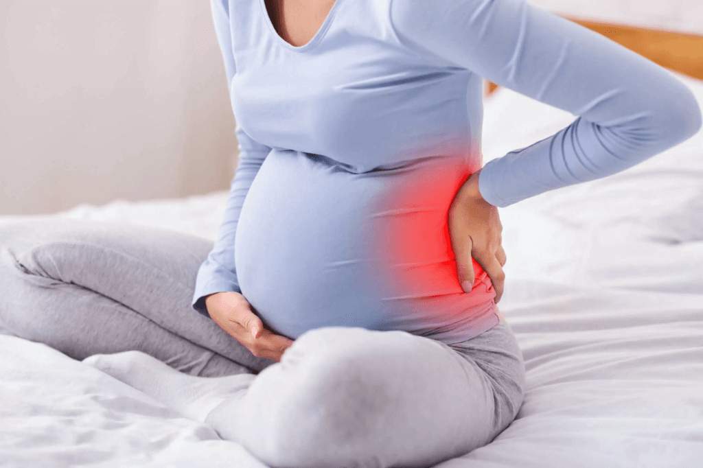 Pregnant woman with baby bump holding lower back with red pain highlight at Zen Physiotherapy Nashik
